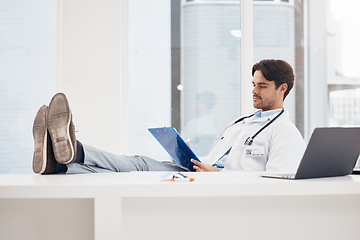 Image showing Doctor, man and relax with feet on desk, reading checklist or thinking on break in hospital office. Medic, document or paperwork for report, results or idea in problem solving, solution or healthcare