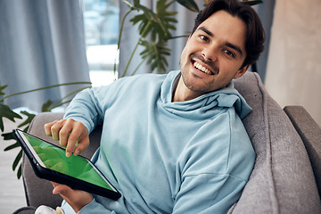 Image showing Portrait, tablet and green screen with a man gaming on a sofa in the living room of his home to relax. Technology, smile and happy young gamer using a display with tracking markers in his apartment
