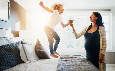 Image showing Family, pregnant woman and her son jumping on the bed while in their home together. Flare, love or smile and a boy child playing in the bedroom with his happy parent for freedom, fun or bonding