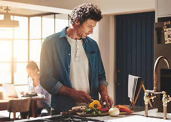 Image showing Cooking, food and man cutting vegetables in the kitchen for diet, healthy or nutrition dinner. Recipe, book and mature male person from Canada chop ingredients for a supper or lunch meal at home.