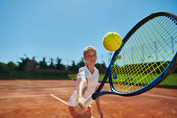 Image showing Close up photo of a young girl showing professional tennis skills in a competitive match on a sunny day, surrounded by the modern aesthetics of a tennis court.