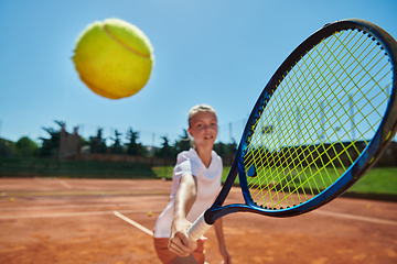 Image showing Close up photo of a young girl showing professional tennis skills in a competitive match on a sunny day, surrounded by the modern aesthetics of a tennis court.