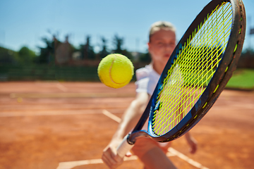 Image showing Close up photo of a young girl showing professional tennis skills in a competitive match on a sunny day, surrounded by the modern aesthetics of a tennis court.