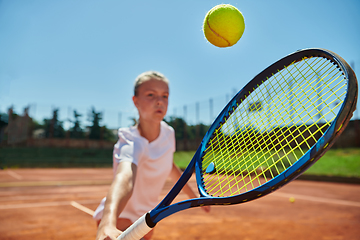 Image showing Close up photo of a young girl showing professional tennis skills in a competitive match on a sunny day, surrounded by the modern aesthetics of a tennis court.