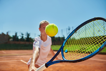 Image showing Close up photo of a young girl showing professional tennis skills in a competitive match on a sunny day, surrounded by the modern aesthetics of a tennis court.