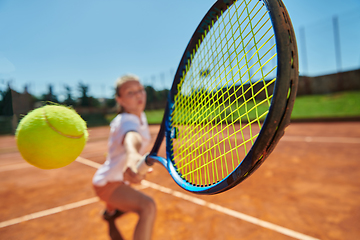 Image showing Close up photo of a young girl showing professional tennis skills in a competitive match on a sunny day, surrounded by the modern aesthetics of a tennis court.