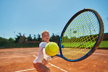 Image showing Close up photo of a young girl showing professional tennis skills in a competitive match on a sunny day, surrounded by the modern aesthetics of a tennis court.