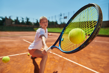 Image showing Close up photo of a young girl showing professional tennis skills in a competitive match on a sunny day, surrounded by the modern aesthetics of a tennis court.