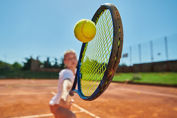 Image showing Close up photo of a young girl showing professional tennis skills in a competitive match on a sunny day, surrounded by the modern aesthetics of a tennis court.