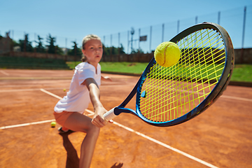 Image showing Close up photo of a young girl showing professional tennis skills in a competitive match on a sunny day, surrounded by the modern aesthetics of a tennis court.