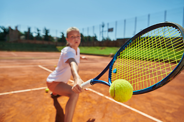 Image showing Close up photo of a young girl showing professional tennis skills in a competitive match on a sunny day, surrounded by the modern aesthetics of a tennis court.