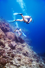 Image showing Couple, swimming and scuba diving in ocean for underwater adventure and explore on tropical holiday or vacation. Sports people, tourist or diver with bubbles, blue water and search sea life or coral