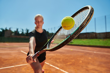 Image showing Close up photo of a young girl showing professional tennis skills in a competitive match on a sunny day, surrounded by the modern aesthetics of a tennis court.