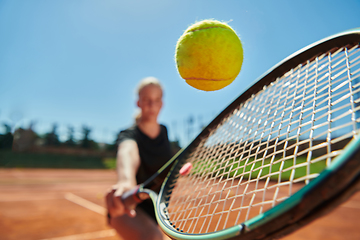 Image showing Close up photo of a young girl showing professional tennis skills in a competitive match on a sunny day, surrounded by the modern aesthetics of a tennis court.