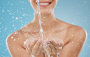 Image showing Skincare, water and hands on blue background in studio for hydration, refreshing and facial cleanse. Splash, wellness and woman ready to clean face for washing, moisturizing and hydrate healthy skin