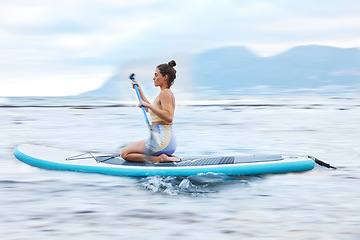 Image showing Paddle board, sea and fitness with a sports woman floating on water in nature for wellness or exercise. Earth, training and travel with a female athlete on a paddleboard while on vacation for travel