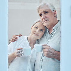 Image showing Love, coffee and senior couple at a window in their home, relax and hug while looking out together. Glass, family and mature man and woman drinking tea, enjoying retirement and view from their house