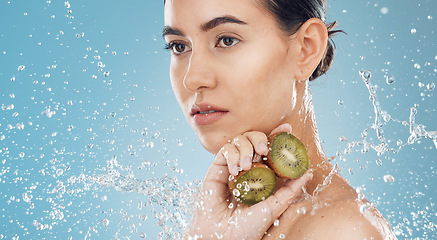 Image showing Beauty, water and kiwi with a model woman posing in studio on a blue background for natural skincare with a splash. Food, wet and luxury with an attractive female posing to promote health or wellness