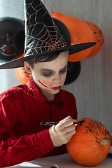 Image showing Happy teen boy in costume drawing a pumpkin for the Halloween celebration.