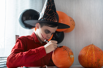 Image showing Happy teen boy in costume drawing a pumpkin for the Halloween celebration.