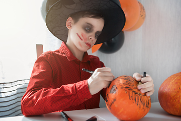 Image showing Happy teen boy in costume drawing a pumpkin for the Halloween celebration.