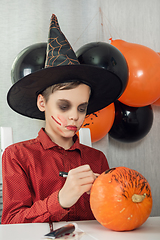 Image showing Happy teen boy in costume drawing a pumpkin for the Halloween celebration.