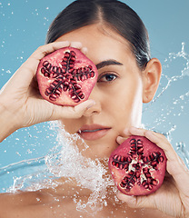 Image showing Face, skincare and pomegranate in woman hands with water splash for facial organic, eco friendly or vegan product in studio blue mock up. Model with fruits for glow skin care promotion or advertising