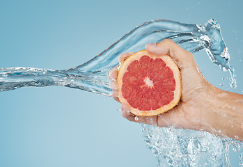 Image showing Grapefruit, water and hand with a summer food for health, nutrition and diet against a blue mockup studio background. Splash, tropical and person cleaning a citrus fruit for snack with mock up space