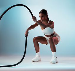 Image showing Woman, battle rope and exercise on blue background in studio resistance training, energy sports or cardio workout. Personal trainer, fitness model or person with wellness health goals for arm muscles