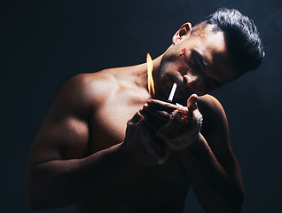 Image showing Dark, flame and man lighting a cigarette with a lighter to smoke after a fight in a studio. Young, dangerous and smoker or fighter from Puerto Rico smoking tobacco isolated by a black background.