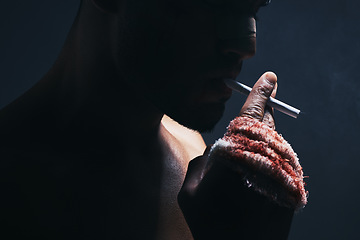 Image showing Injury, cigarette and blood bandage on hand of kickboxing man in studio for shadow, art deco and bad habits background. Male champion boxer smoking after fighting in MMA violence sports competition