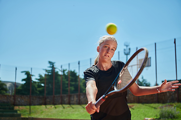 Image showing Close up photo of a young girl showing professional tennis skills in a competitive match on a sunny day, surrounded by the modern aesthetics of a tennis court.