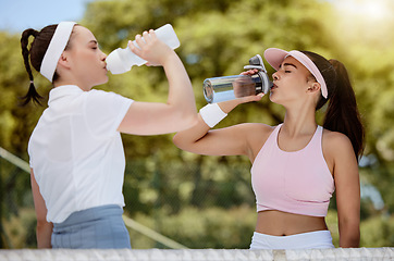 Image showing Tennis, fitness and water, women drinking from bottle on court in hot summer sun at match. Sports exercise, healthy friendship and training workout, girl friends drinking water at competition or game