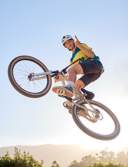 Image showing Bike, jump and rock on hand sign with a man bmx rider jumping over a ramp on a trail or course in nature. Sky, mountain and cycling with a male athlete jumping in mid air during fitness exercise