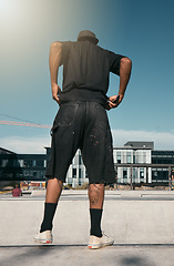 Image showing Skate clothes, urban fashion and man with emo, goth or gen z contemporary street style at fitness skate park for training. Blue sky lens flare, concrete building and back view of stylish black person