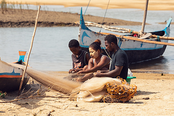 Image showing Fisherman and woman repairing fishing nets at the estuaries of a river. The woman has a traditionally Malagasy painted face