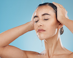 Image showing Shower, water and woman cleaning her body on a blue studio background. Bodycare, haircare and health or wellness with a young female cleansing her face, getting wet for fresh and cosmetic skin