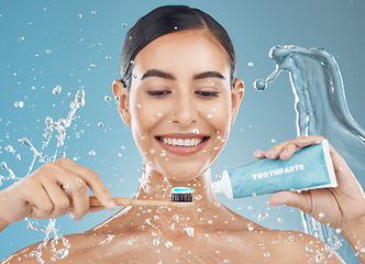 Image showing Woman, brushing teeth and with smile, happy and water splash for wellness, dental care and with blue studio background. Oral hygiene, young female and girl being confident, toothpaste and tooth brush