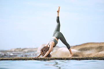 Image showing Yoga, stretching and black woman doing exercise at the beach, in yoga pose by water and rocks. Fitness, motivation and girl doing workout, training and exercising by sea for peace, wellness and calm