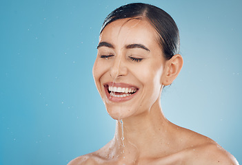 Image showing Skincare, cleaning and washing face by woman in studio for wellness, shower, happy and relax against a blue background mockup. Girl, water and face with model face wash for beauty, splash and skin