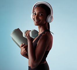 Image showing Woman, dumbbells and music headphones for workout in studio on blue background for yoga mat training, exercise or pilates. Portrait, smile or happy fitness model with weights, radio or health podcast