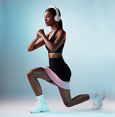 Image showing Woman, music headphones or resistance band workout on blue background in studio for training, exercise or gym. Personal trainer, person or fitness model with health goals, radio or motivation podcast