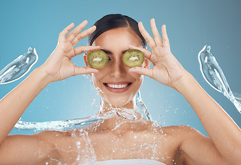 Image showing Woman, shower and kiwi for beauty, skincare and eye treatment in a studio with mockup and blue background. Fruit, water and wellness girl model relax, happy and smile with organic, shower and product