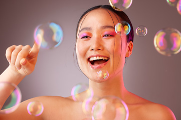 Image showing Beauty, bubbles and Asian woman with bright eyeshadow isolated on a studio background. Fun, glamour and colourful cosmetics with a beautiful Chinese woman popping bubbles for a healthy, fresh skin