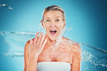 Image showing Beauty splash, senior woman and wow face in studio for cleaning, fresh and grooming on blue background. Skincare, water splash and elderly lady model shocked by water, hydration and moisture product