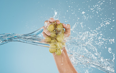 Image showing Hand, grapes and water by woman in studio for wellness, health and nutrition mockup, studio and blue background. Splash, fruit and model hands for plant, organic and nutrition skin, product and diet