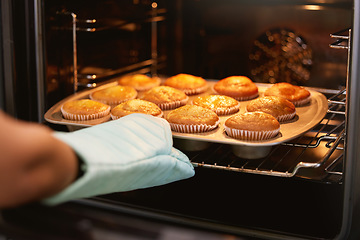 Image showing Hand, oven and muffins in baking, food or cooking sweet delicious cakes on a tray at home in the kitchen. Hands of baker taking hot muffin baked meal, treat or delight in pastry making at the house