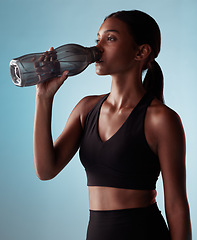 Image showing Fitness woman drinking water bottle in studio, training and workout, exercise or sports challenge on blue background. Thirsty young athlete, hydration rest or wellness, healthy lifestyle or nutrition