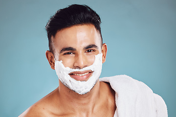 Image showing Face, beauty and shaving with a man model in studio on a blue background for wellness or grooming. Portrait, skincare and hair removal with a handsome young male in the bathroom to shave his beard