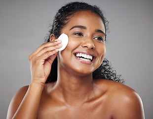 Image showing Skincare, cotton pad and woman cleaning face with a smile against a grey studio background. Clean, wellness and African girl model thinking of facial makeup, cosmetic cleansing and care for skin